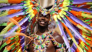 A man wearing an outfit of purple, yellow, green and orange feathers at Notting Hill Carnival