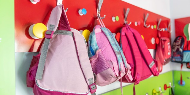 Pink and red schoolbags hanging on hooks in a classroom