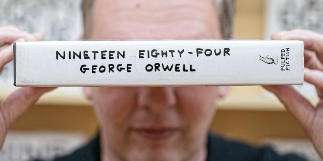 The artist David Shrigley holding a copy of 1984 by George Orwell over his eyes