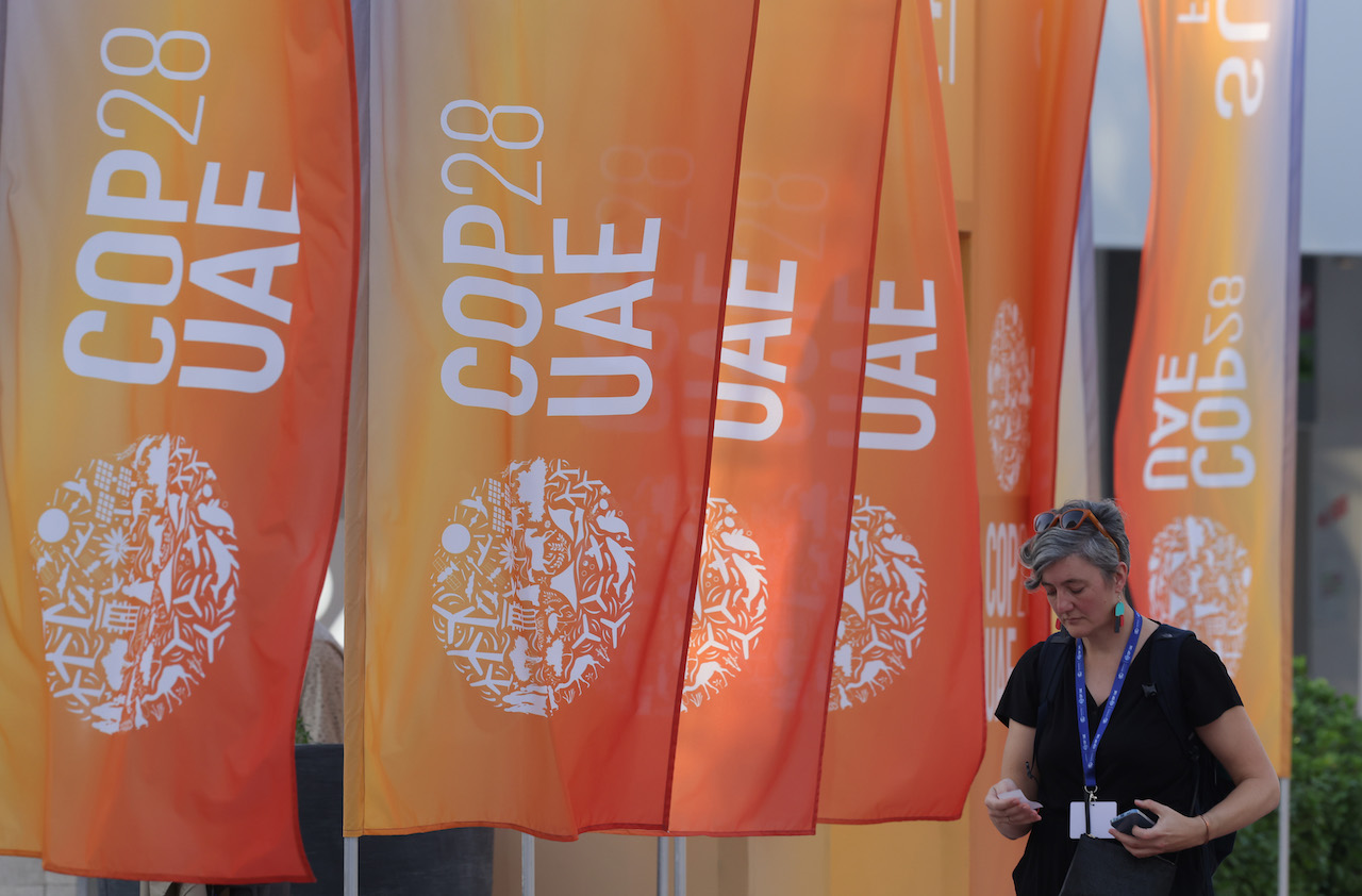 A woman walks in dubai in front of orange COP28 banners.