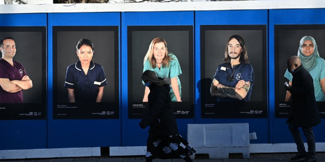 NHS staff posters on a wall with people walking past