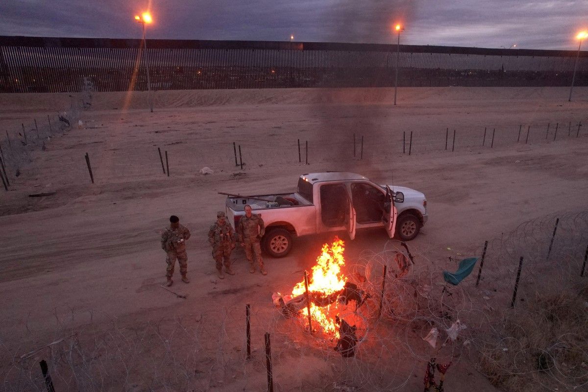 File image taken from Ciudad Juarez, Mexico, showing members of the Texas National Guard next to a burning pile of migrants' belongings on the razor wire fence at the border.