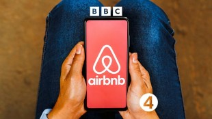 A woman holds a mobile phone displaying the Airbnb app