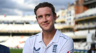 Bowler Stuart Broad wears his England cricket strip at a cricket ground. He is smiling and looking up and to the left