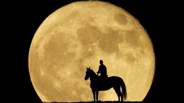 A man sits on his horse and looks at the super moon known as the Blue Moon, from a mountain in Mogan on the south of the island of Gran Canaria, Spain