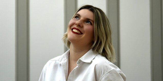 Jess Warren wears a white shirt and red lipstick and smiles as she looks up 