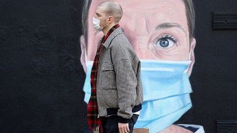 A man walks past a mural in Manchester of a woman wearing a mask