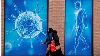 Women walk past a poster depicting a virus