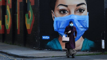 A woman wearing a mask walks past graffiti art praising the NHS