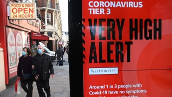 Shoppers walk by a "vert high alert" warning sign in London on 17 December 2020