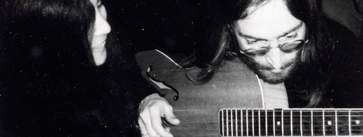 John Lennon plays the guitar, with Yoko Ono looking on