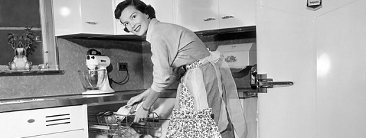 Black and white archive image of a woman wearing an apron while loading a dishwasher {George Marks/Getty Images}