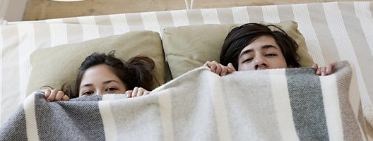 A couple hide under bed covers