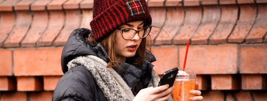 A woman in a woolly hat looks, unimpressed at a smartphone