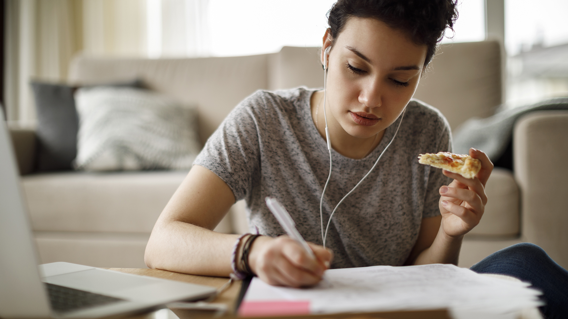 A student eats a slice of pizza while working (Credit: Getty Images)