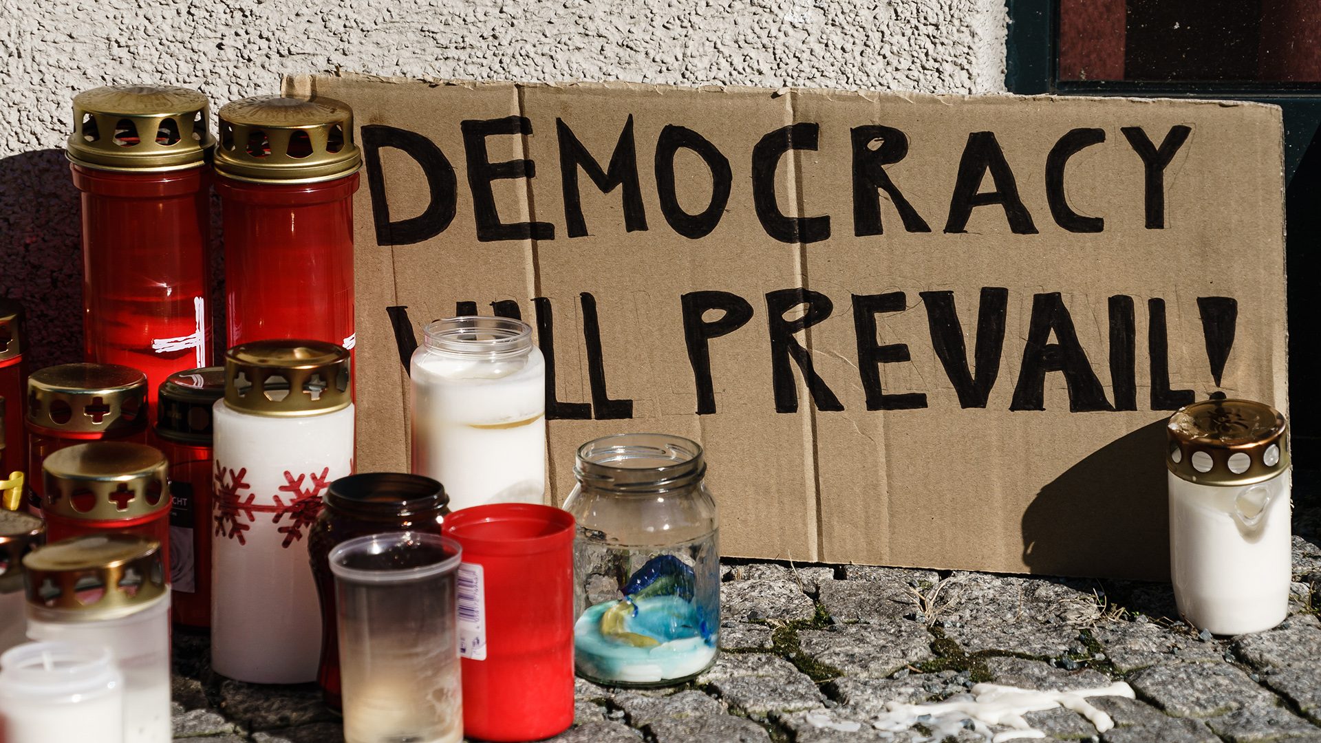 A cardboard sign reading "democracy will prevail" stands next to mourning candles in front of the Ukraine embassy in Berlin, Germany, 1 March 2022 (Credit: Clemens Bilan/EPA)